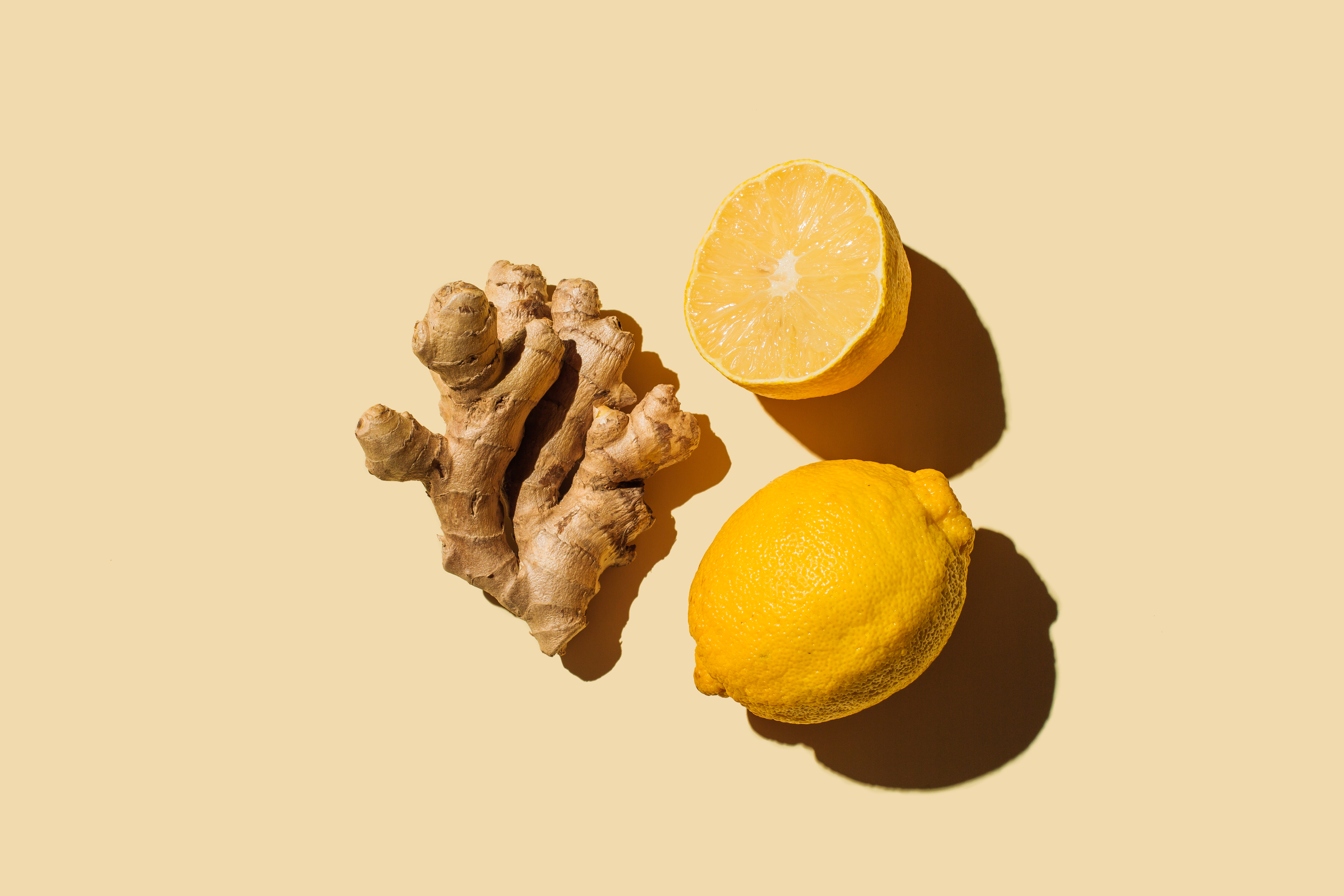 A photo of ginger root next to lemon slices, on a yellow background.